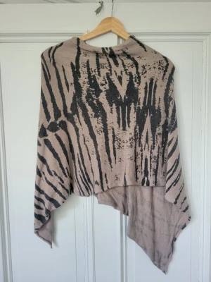 Beige poncho med zebramönster - Snygg beige poncho med svart zebramönster och asymmetrisk form. Så fin att ha över en tröja på sommarkvällar! Väldigt mjuk och mysig! Består av 30% ull/cashmere så värmer på ett helt perfekt sätt!Älskar men rensar garderoben och behöver platsen🩷 är öppen för prisförslag på alla mina annonser så kika gärna! 