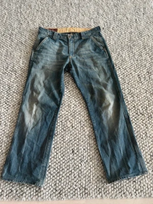 Blå raka "Marlboro Classics" jeans - Säljer ett par blå jeans med rak passform och klassiska fem fickor. Jeansen har snygga slitningar, en läderpatch bak i midjan och med lite bootcut. Perfekta för en avslappnad och cool stil.
