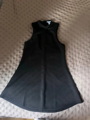 Svart ärmlös klänning med hög krage - En stilren svart klänning med hög krage och ärmlös design. Klänningen har en lätt utställd form och är perfekt för dig som gillar minimalistisk stil. 