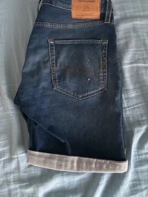 Blå jeansshorts från Jack & Jones - Snygga blå jeansshorts från Jack & Jones med klassisk femficksdesign och uppvikta benslut. Shortsen har normal passform och är tillverkade i mjuk bomull med en mörk tvätt och subtila slitningar. Perfekta för sommardagar!