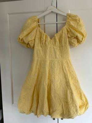 Gul kort klänning med puffärmar - Superfin gul kort klänning med stora puffärmar och v-ringning. Klänningen har ett broderat blommönster och ballongformad kjol. Klänningenr lite ljusare gul än på bild💛 Ny med prislapp kvar!!