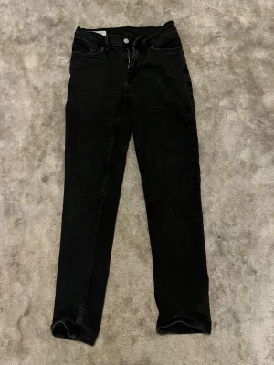 Svarta skinny jeans med hög midja - Svarta skinny jeans med hög midja och klassisk femficksdesign. Jeansen har dragkedjegylf och knapp framtill samt bälteshällor. Materialet är stretchigt för en bekväm passform. Perfekta till sneakers eller boots.
