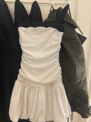 Vit och svart klänning Gina Tricot - Supersöt kort klänning från Gina Tricot i vit och svart ANVÄND 1 gång!! . Klänningen har breda axelband, rynkade sidor och volang nedtill. Materialet är strukturerat och känns lätt, perfekt för varmare dagar. Snygg kontrast mellan svart upptill och vit kjol.