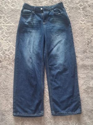Blåa wide leg jeans med hög midja - Säljer ett par blåa jeans med wide leg-modell och hög midja. Jeansen har klassiska fickor fram och bak, samt ljusare tvättade partier på låren för en cool look. Perfekta för dig som gillar avslappnad och trendig stil.