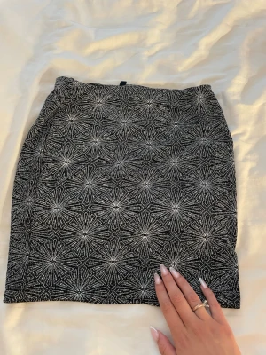 Svartvit mönstrad kortkjol - Kortkjol i svart och vitt med ett geometriskt, nästan stjärnformat mönster. Kjolen har en rak passform och är tillverkad i ett stretchigt material som sitter snyggt på kroppen. Perfekt för dig som gillar grafiska detaljer.