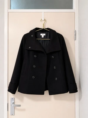 Svart dubbelknäppt rock från H&M - Stilren svart rock från H&M med dubbelknäppning och bred krage. Rocken har två sidofickor, dekorativa knappar på ärmsluten och ett bälte med knappar i ryggen. Klassisk och tidlös modell i vadderat tyg som passar perfekt till höst och vinter.