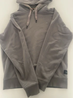 Grå hoodie med huva från Replay - Säljer en stilren grå hoodie från Replay som köptes från NK för 1600kr. Tröjan har ribbade muddar och en diskret logotyp på bröstet. Materialet är mjukt och bekvämt, perfekt för en avslappnad look. Passar dig som gillar enkel och klassisk design.