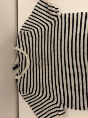 Randig tröja från H&M Divided - Säljer en mysig stickad tröja från H&M Divided i vitt med svarta horisontella ränder. Tröjan har rund halsringning och är tillverkad i ett mjukt material som passar perfekt för lager-på-lager-stil.