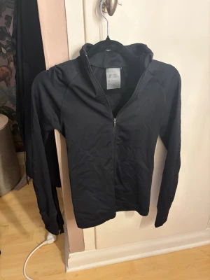 Svart ziptröja från Relode - Svart långärmad ziptröja från Relode med hög krage och dragkedja framtill. Tillverkad i ett stretchigt och mjukt material som passar perfekt till träning eller uppvärmning. Enkel och stilren design utan synliga loggor på framsidan. Säljer för att den är för liten för mig 