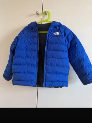 Blå dunjacka från The North Face - Använd en gång men kedjan är trasig! Perfekt för någon som är händig eller vill fixa den. Blå dunjacka från The North Face med huva och dragkedja framtill. Jackan har quiltad design och är lätt vadderad för extra värme. Perfekt för kalla vinterdagar och har en klassisk logga på bröstet. Materialet är syntet med dunfyllning.