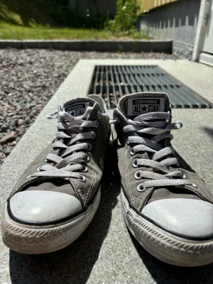 Grå Converse All Star låga sneakers - Klassiska Converse All Star sneakers i grå canvas med vita gummisulor i ett otroligt bra skick. Skorna har vita snören och metallfärgade öljetter.