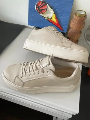 Beige sneakers från Vagabond - (Priset kan diskuteras)Stilrena beige sneakers från Vagabond med klassisk låg profil och rund tå. Skorna är tillverkade i slätt läder och har matchande beige snörning samt en tjock vit sula för en modern look. Perfekta för dig som gillar minimalistisk och clean stil.