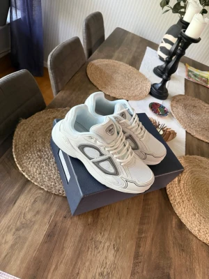 Vita Dior B30 sneakers - Snygga vita Dior B30 sneakers med mesh och läderdetaljer. Skorna har en chunky sula och coola grå och svarta inslag på sidorna. Klassisk snörning och logga på plösen. Perfekta för dig som gillar exklusiv streetwear.
