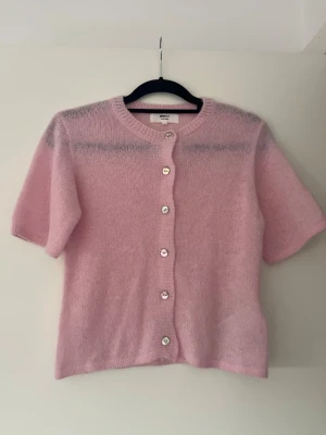 Ljusrosa kofta med kort ärm - Supersöt ljusrosa kofta från gina tricot med korta ärmar och rund hals. Koftan är stickad i ett fluffigt material och har pärlemorknappar framtill. Perfekt att slänga över en topp för en mjuk och trendig look.