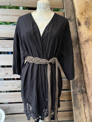 Fin! Svart kimono med vida ärmar och spets - Svart blus/kofta i kimonomodell med vida ärmar och v-ringad hals och dekorativ spetsdetalj längst ner. Materialet är lätt och luftig bomull,  perfekt för chill dagar hemma, till linne och jeansshorts eller på stranden ovanpå bikini. Inte mycket använd så i fint skick. Skärpet på bilden igår ej. Stl one size, skulle säga 36-42 beroende på hur man vill att den ska sitta.