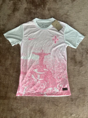 Nike Dri-Fit fotbollströja rosa/vit M - Säljer en snygg Nike Dri-Fit fotbollströja i vitt och ljusrosa med motiv av Kristusstatyn i Rio de Janeiro. Tröjan har korta ärmar, rund hals och är tillverkad i ett lätt, ventilerande funktionsmaterial. Perfekt för träning eller match! Rio De Janeiro Version. Storlek M utan person/nummer på ryggen. Pris kan diskuteras. 😊