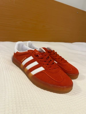 Adidas Gazelle röda sneakers - Snygga Adidas Gazelle sneakers i rött mocka med klassiska vita ränder på sidorna och vit häl. Helt nya, bara testade! Storlek 42+2/3. Kom med bud och frågor.