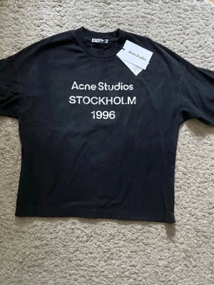 Svart Acne Studios t-shirt - Cool svart t-shirt från Acne Studios med vit text 'STOCKHOLM 1996' på bröstet. Klassisk passform med rund hals och korta ärmar. Perfekt för dig som gillar stilrena och trendiga plagg med streetkänsla. Priset kan diskuteras 