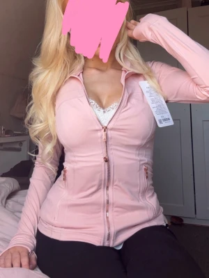 Äkta lululemon ljusrosa träningsjacka med dragkedja - Snygg ljusrosa äkta lululemon träningsjacka med hel dragkedja och två fickor med dragkedjor som är i roseguld. Jackan har en slim passform och långa ärmar med tumhål. Perfekt för gymmet eller löprundan.  Jag har köpt den på semester och det står att det är storlek 2, men den passar mig som använder xs/s i vanliga fall. Den hade även nog kunnat passa en M. Skriv för mått eller andra frågor❤️ Jag säljer 2 st! Och det finns en svart uppe på min profil