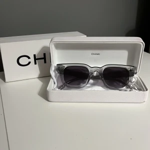 CHIMI 04 - Snygga solglasögon från CHIMI i transparent grå plast med fyrkantig form och mörka glas. Kommer med originaletui och box. Perfekta för att lyfta din stil året runt.