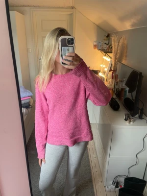 Rosa stickad tröja med rund hals - Mysig rosa stickad tröja med avslappnad passform och rund halsringning. Tröjan har långa ärmar och ribbade muddar vid ärmslut och nederkant. Perfekt för dig som gillar en enkel men färgglad stil.