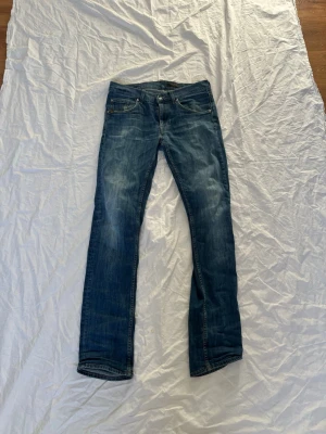 Blå raka jeans med slitningar - Snygga blå jeans med raka ben och diskreta slitningar på låren. Klassisk femficksmodell med knapp- och dragkedjegylf. Jeansen har en läderpatch bak i midjan och är tillverkade i bomullsdenim. Perfekta för en avslappnad och trendig look.