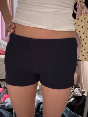 Mörkblå ribbade stickade shorts - Säljer ett par mörkblå stickade shorts med bred ribbad midja och ribbade detaljer vid benslut. Shortsen har en högmidjad passform och är perfekta för en avslappnad och trendig look.