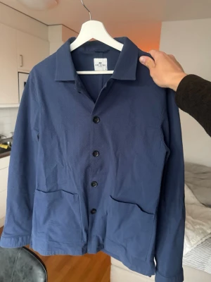 John Henric overshirt blå  - Snygg blå overshirt från John Henric i strukturerad bomull. Klassisk krage, knäppning framtill med svarta knappar och två stora fickor framtill. Perfekt lager-på-lager-plagg med avslappnad passform och stilren look., nypris 999-1299.  