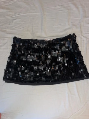 Svart paljettkjol från Gina Tricot - Snygg svart kortkjol från Gina Tricot täckt med glittriga paljetter. Kjolen har en rak passform och är perfekt för dig som vill sticka ut. Materialet är polyester och kjolen har en bekväm midja.