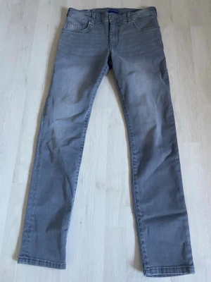 Gråa slim fit jeans, Scotch&Soda - Snygga gråa slim fit jeans med klassisk femficksdesign och raka ben av Scotch&Soda. Jeansen har diskreta sömmar och en neutral tvätt som passar till det mesta. Tillverkade i mjukt denimtyg för skön känsla och stilren look. Använd några gånger för att testa dom. Frågor eller funderingar kan ni höra av er!