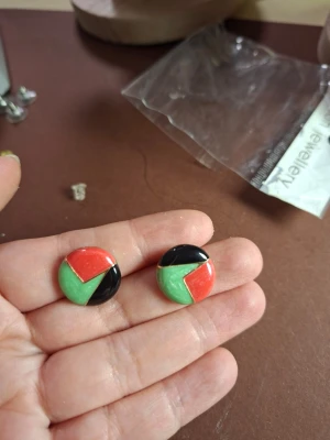 Runda örhängen i rött, grönt och svart - Säljer ett par coola runda örhängen med geometriskt mönster i rött, grönt och svart. Örhängena är tillverkade i plast och har en blank finish som ger dem en modern look. Perfekt för dig som gillar färg och unika accessoarer.