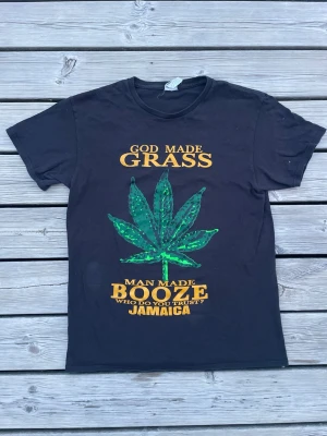 Rolig t-shirt! - Svart t-shirt med stort grönt blad-tryck och gul text: 'God made grass, man made booze, who do you trust? Jamaica'. Klassisk rund hals och korta ärmar. Perfekt för dig som gillar statement-plagg. Perfekt nu till sommaren, fråga vid intresse, priset står kvar!