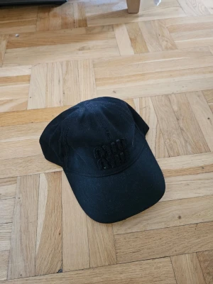 Miu Miu denim keps med broderad text - Svart Miu Miu keps i klassisk modell med böjd skärm och justerbar rem baktill. Framtill finns en diskret broderad text i svart. Perfekt accessoar för en avslappnad och stilren look.