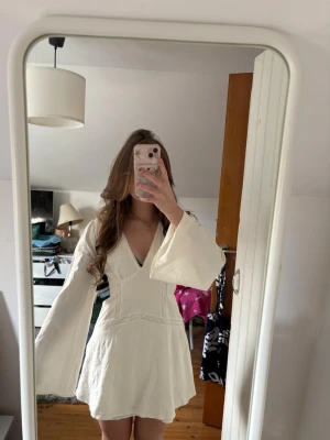 Studentklänning  - Supersöt vit kort klänning med v-ringning och vida långa ärmar. Klänningen har spetsdetaljer och en lätt utsvängd kjol. Oanväd och säljer då jag har en annan klänning till studenten!🩷 