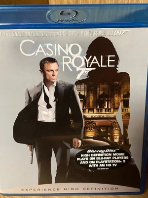Casino Royale Blu-ray - Casino Royale på Blu-ray, en James Bond-film med Daniel Craig. Omslaget är blått och har en stilren design med Bond i kostym och siluett av en kvinna. Filmen har bonusmaterial och flera ljudspår, inklusive svenska och engelska. Perfekt för filmkvällar och samlare.
