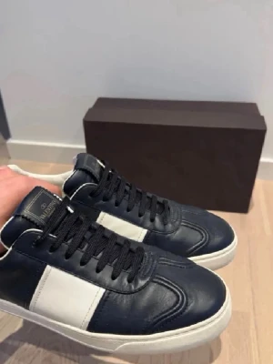 Valentino flycrews sneakers blå/vit - Snygga sneakers från Valentino flycrews i blått och vitt läder med svarta skosnören. Klassisk låg modell med vita detaljer och coola nitar baktill på sulan. Perfekta för dig som vill sticka ut med stilrena och exklusiva skor.