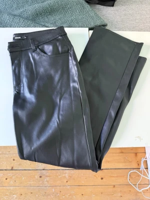 Svarta skinnbyxor från BikBok - Snygga svarta skinnbyxor från BikBok i storlek 42. Byxorna har klassisk femficksdesign, lite slitage men annars inget annat!