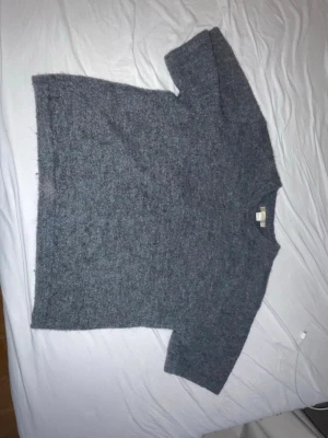 Grå stickad tröja från Gina Tricot - Mysig grå stickad tröja från Gina Tricot med rund halsringning och avslappnad passform. Tröjan har långa ärmar och är tillverkad i ett fluffigt, mjukt material som passar perfekt för kyligare dagar.