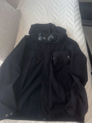 Svart C.P. Company vindjacka med goggles - Svart vindjacka från C.P. Company med ikoniska goggles i huvan.  Köptes i butik. Använt den cirka ett halv år nu.