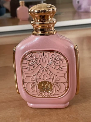 Zimaya Zukhruf Femme Eau de Parfum - Lyxig parfymflaska i skimrande rosa med gulddetaljer och vackert orientaliskt mönster. Zukhrof Femme från Zimaya, 100 ml eau de parfum, tillverkad i Förenade Arabemiraten. Flaskan har en exklusiv och dekorativ design som sticker ut i parfymhyllan. Endast testad!