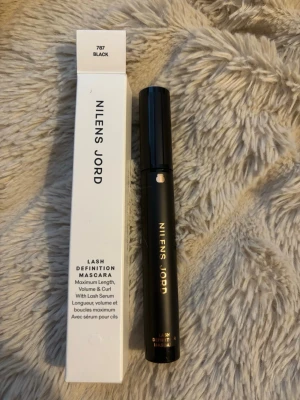 Nilens Jord Lash Definition Mascara - Nilens Jord Lash Definition Mascara i färgen svart ger maximal längd, volym och böj till fransarna. Kommer i en elegant svart tub med guldtext och tillhörande vit förpackning. Innehåller fransserum för extra vård.