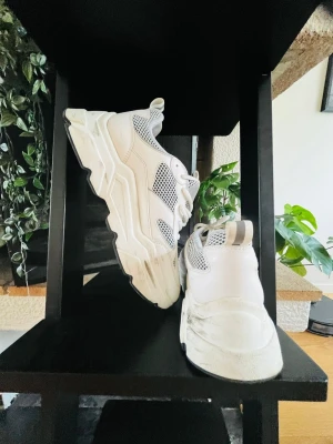 Chunky vita sneakers med meshdetaljer - Säljer ett par chunky vita sneakers med grå meshdetaljer och tjock sula. Skorna har sportig vibe, snörning och dragflik bak. Perfekta för dig som gillar streetstyle och vill sticka ut med en modern look.