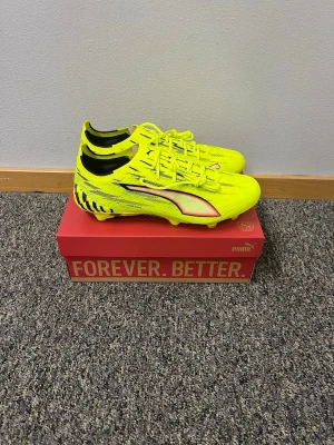 Gula Puma fotbollsskor med svart detalj - Säljer ett par grymma fotbollsskor från Puma i neon-gult med svarta och vita detaljer. Skorna har snörning, låg profil och är tillverkade i syntetmaterial för bästa grepp och känsla på planen. Perfekta för dig som vill sticka ut och ha full kontroll på bollen.