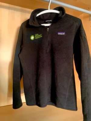 Svart fleece-tröja från Patagonia - Svart långärmad fleece-tröja från Patagonia med halv dragkedja framtill och broderad Oak Street Health-logga på bröstet. Tröjan har hög krage och en ficka med dragkedja på ärmen. Perfekt för kyliga dagar. Skick: Mycket bra | Storlek: M | Bara & skriva om ni har några frågor!!!!😊