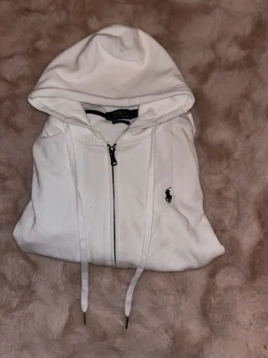 Vit hoodie från Polo Ralph Lauren - Säljer en clean vit hoodie från Polo Ralph Lauren med dragkedja, huva och dragsnören. Priset är lågt eftersom som att det finns LITE smuts på den som självklart går att ta bort.