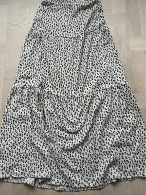 Leopardmönstrad kjol - Leopardmönstrad kjol från Kappahl i beige och svart. Klänningen har en avslappnad passform och är tillverkad i ett mjukt, lätt material som passar perfekt för varmare dagar. Den har volangdetaljer och ett trendigt djurmönster. I storlek 152cm🐆