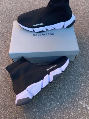 Speed Trainer svarta sneakers - Svarta Speed Trainer sneakers med vit chunky sula och stickad ovandel i textil. Strumpliknande passform och diskret logga på sidan. Sulan är futuristisk och ger en sportig vibe. Perfekta för dig som gillar streetwear och vill sticka ut.