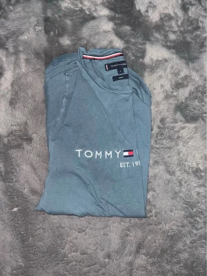 Tommy Hilfiger Est. 1985 T-shirt - stilren t-shirt från Tommy Hilfiger i en snygg blågrå nyans. den lilla flaggan på ärmen.   Slim Fit, Sitter riktigt snyggt och följsamt.  Toppskick och fräsch. 