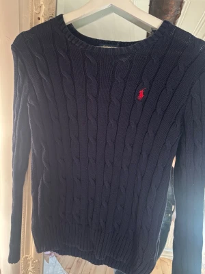 Mörkblå kabelstickad tröja Polo Ralph Lauren - Kabelstickad mörkblå tröja från Polo Ralph Lauren i mjuk pima bomull. Jag vet att jag lagat ett litet hål men just nu hittar jag inte det😊