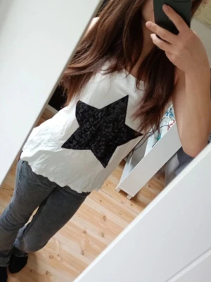 Vit linnetopp med svart paljettstjärna - Snygg vit linnetopp med en stor svart stjärna i paljetter framtill. Modellen är ärmlös med djup urringning och avslappnad passform. Perfekt att styla med jeans eller shorts för en cool look💗